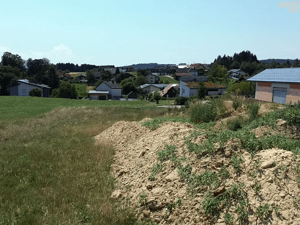 Blick über ein Feld mit Erdhaufen auf eine ländliche Siedlung im Hintergrund.