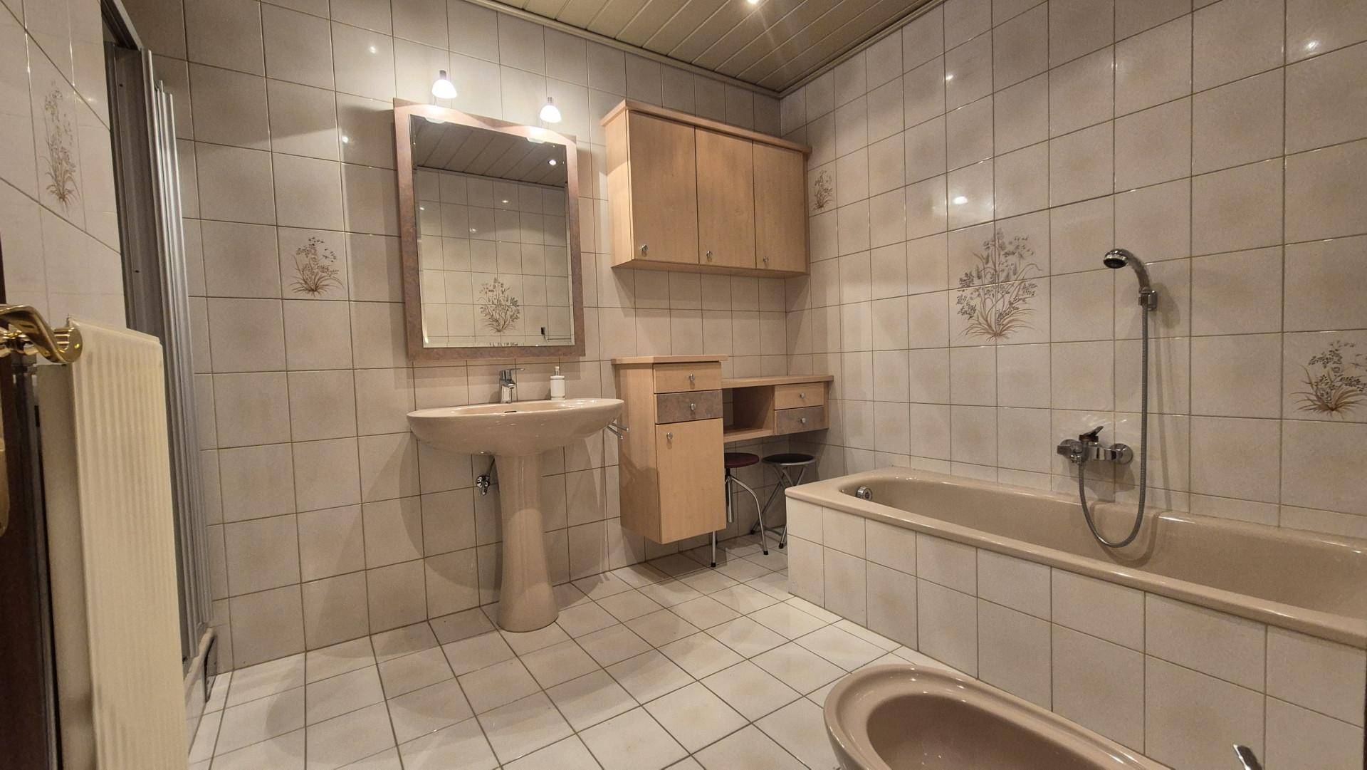 Gefliestes Badezimmer mit Badewanne, Waschbecken und Bidet in hellem Design.