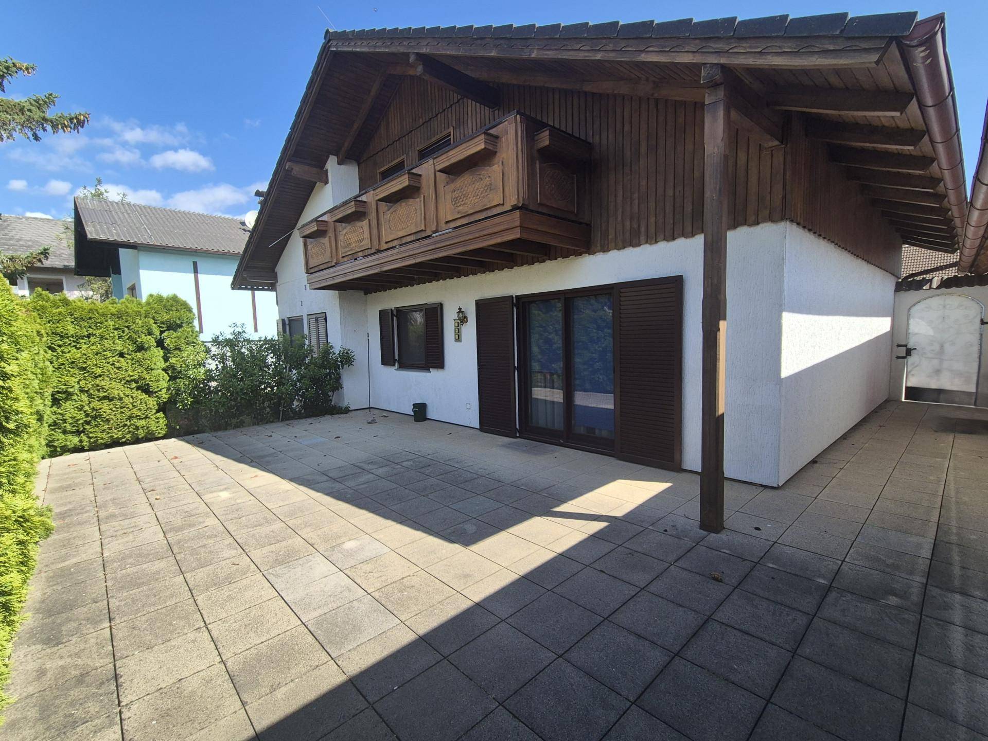 Geräumige gepflasterte Terrasse am Haus mit Zugang zum Garten und Holzbalkon darüber.