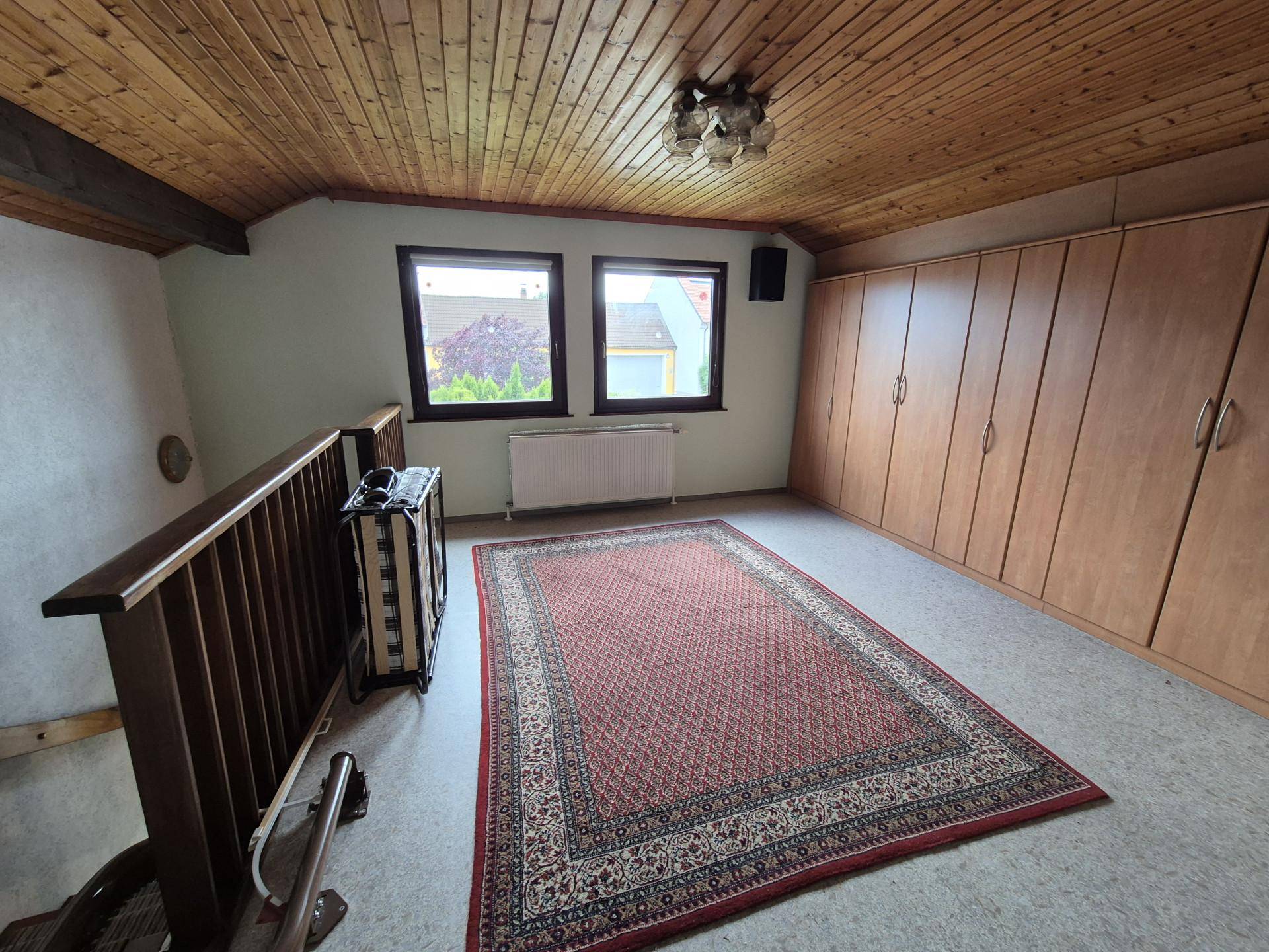 Dachgeschossraum mit Holzdecke, Einbauschränken und Teppichboden, hell durch zwei Fenster.