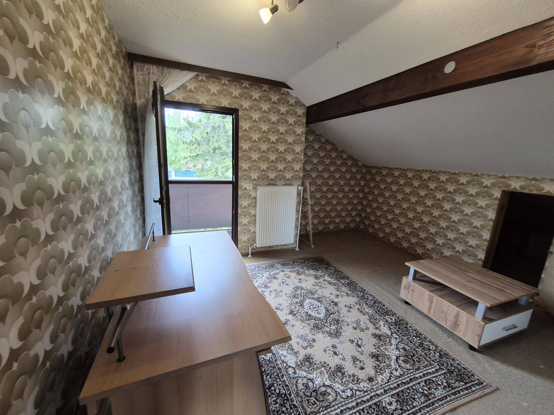 Dachgeschosszimmer mit gemusterter Tapete, Holzbalken und Zugang zu einem französischen Balkon.
