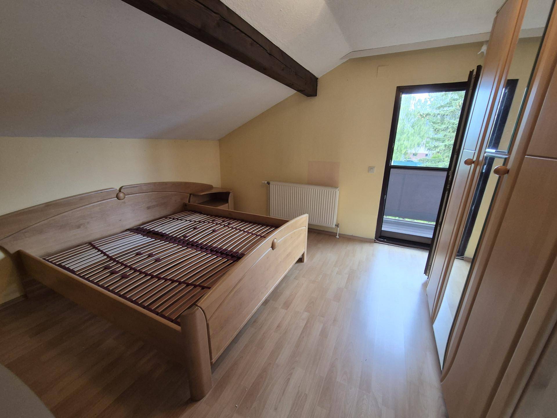 Helles Schlafzimmer im Dachgeschoss mit Holzboden, Bett und Zugang zu einem Balkon.