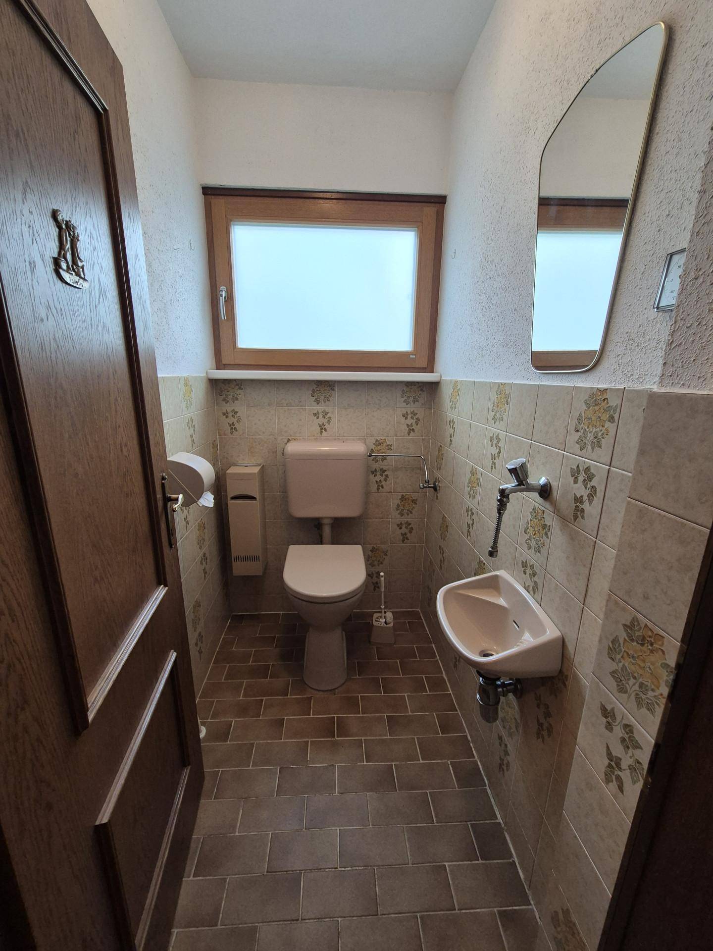 Kleines Gäste-WC mit Fenster, beigen Fliesen und einem Waschbecken.
