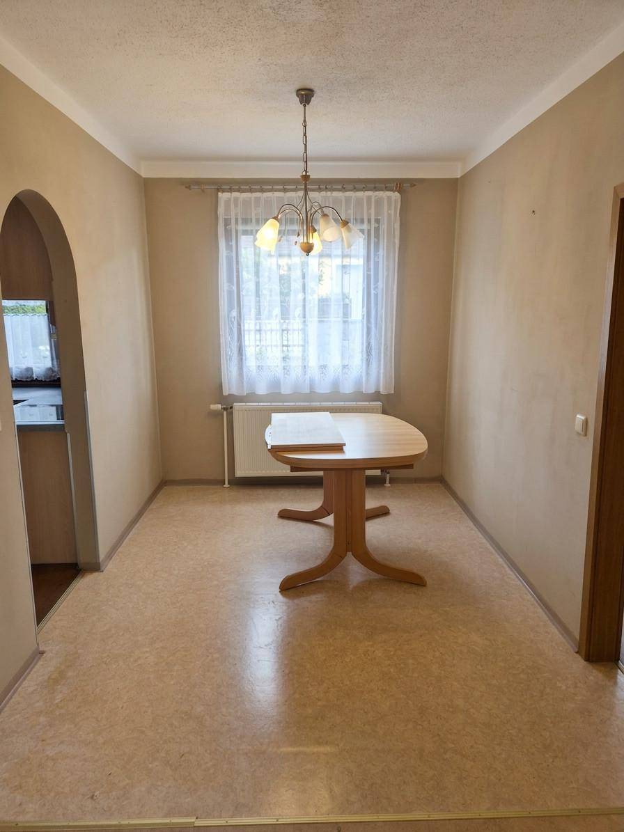 Heller Essbereich mit einem Holztisch, Fenster und Zugang zur Küche durch einen Bogen.