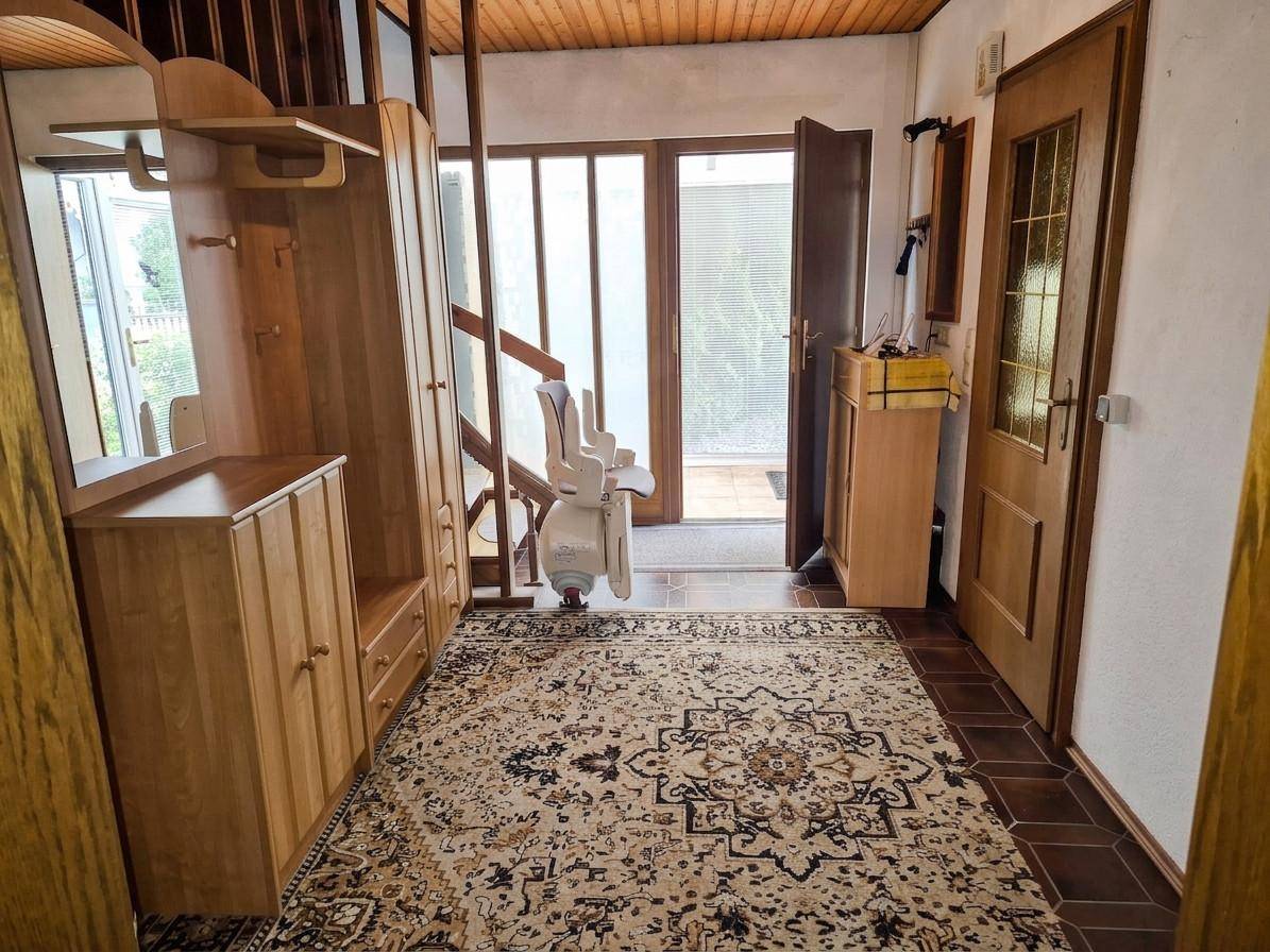 Eingangsbereich mit Holzmöbeln, Teppich und einem Treppenlift zur oberen Etage.