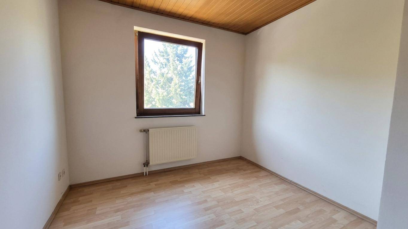 Kleines Zimmer mit Laminatboden, Fenster und Holzpaneeldecke, ideal als Kinder- oder Arbeitszimmer.