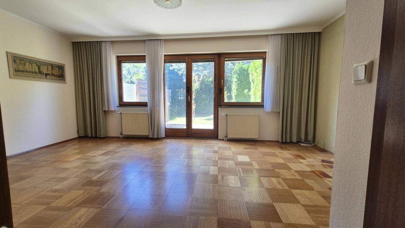 Helles Wohnzimmer mit Parkettboden und großen Fenstern mit Zugang zum Garten.
