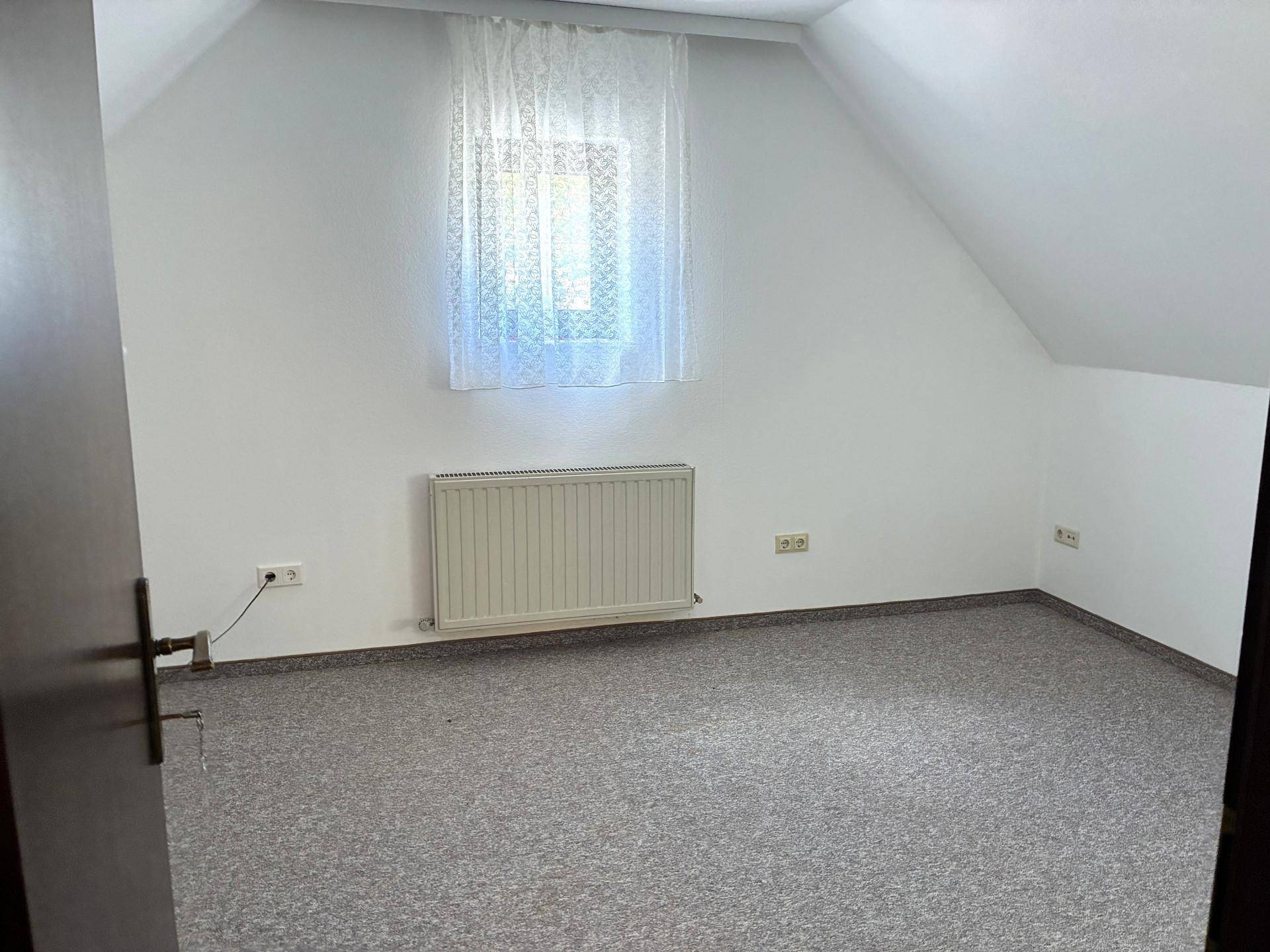Helles Zimmer im Dachgeschoss mit grauem Bodenbelag und einem kleinen Fenster.