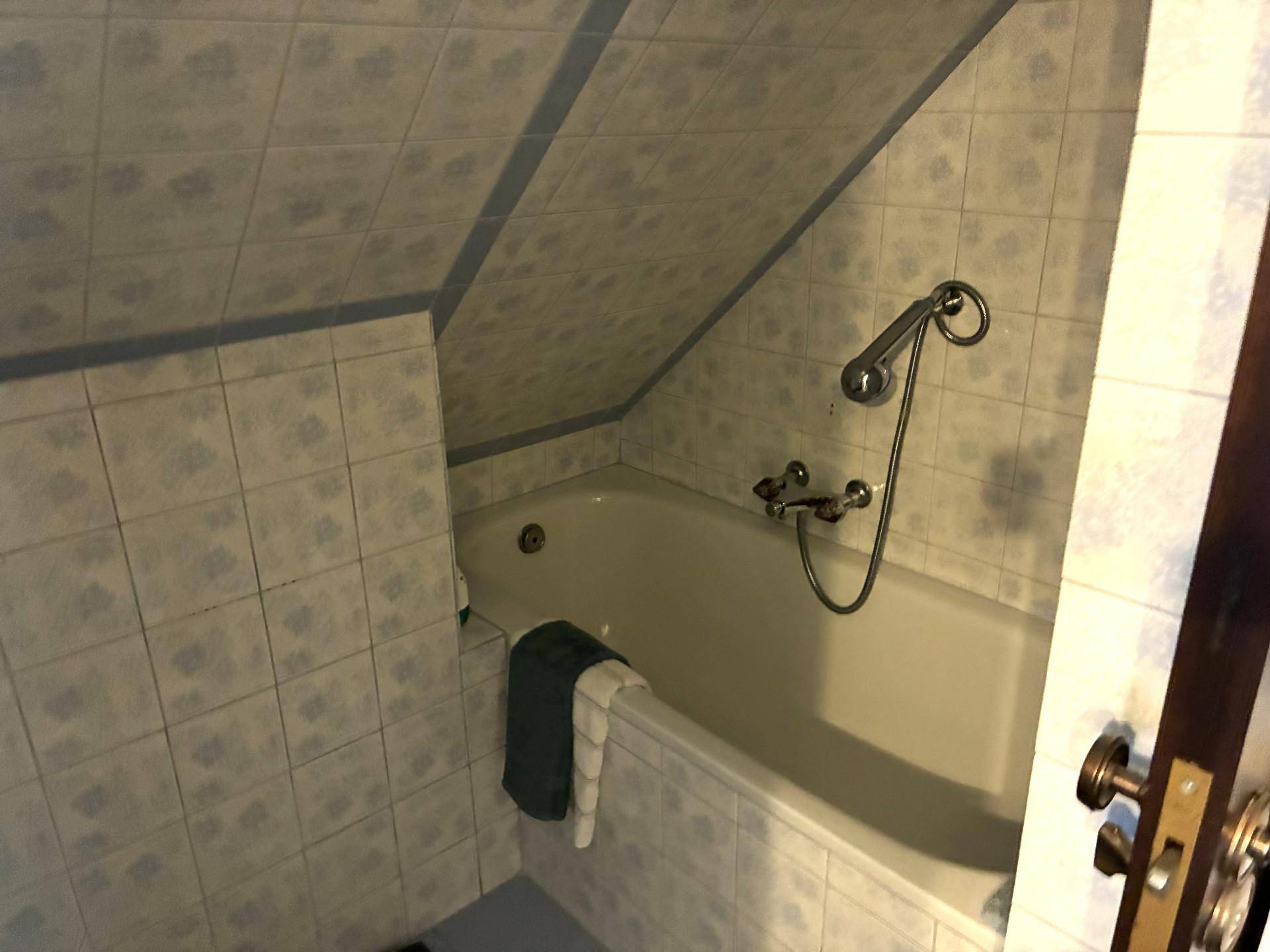 Detailansicht der Badewanne im gefliesten Badezimmer mit schräger Dachschräge.