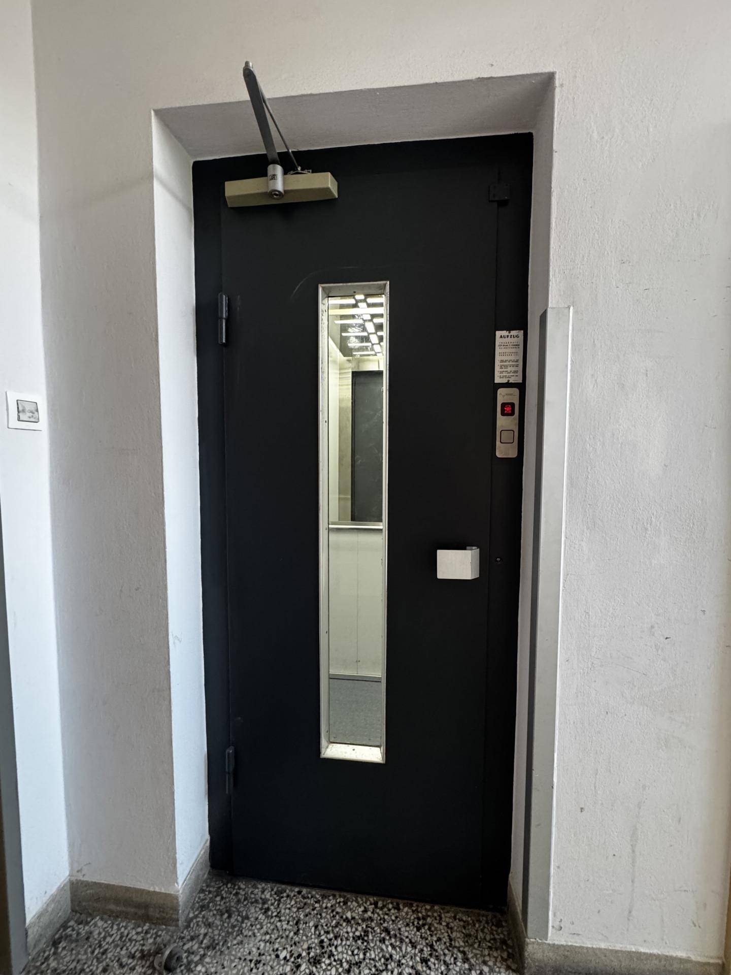 Schwarze Aufzugstür in einem Flur mit einem kleinen Fenster.