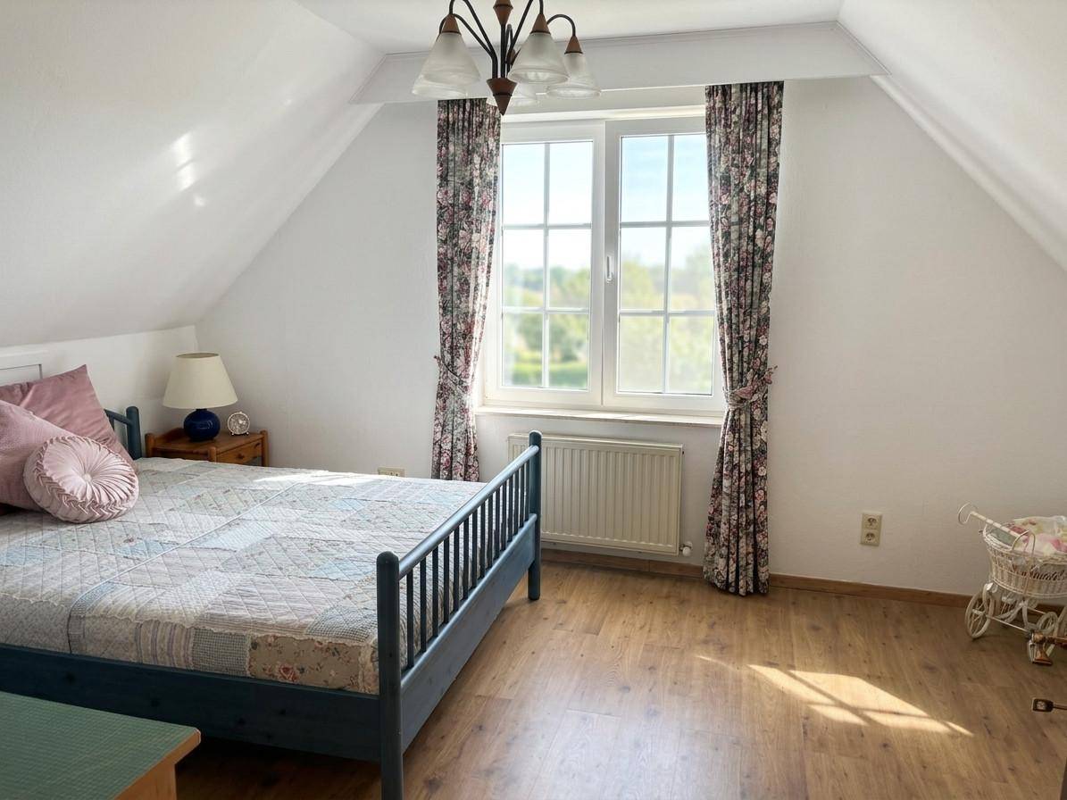 Schlafzimmer im Dachgeschoss mit Holzboden, Doppelbett und großem Fenster mit grüner Aussicht.
