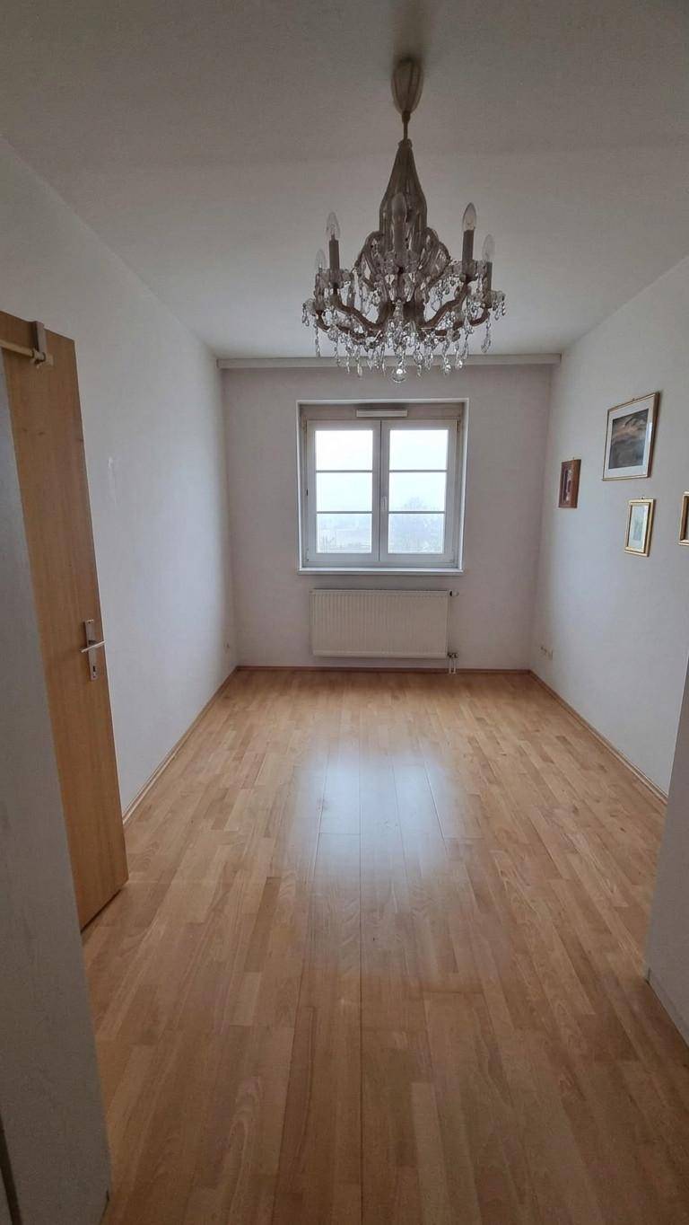 Heller Raum mit Parkettboden, einem Fenster und einem eleganten Kronleuchter an der Decke.