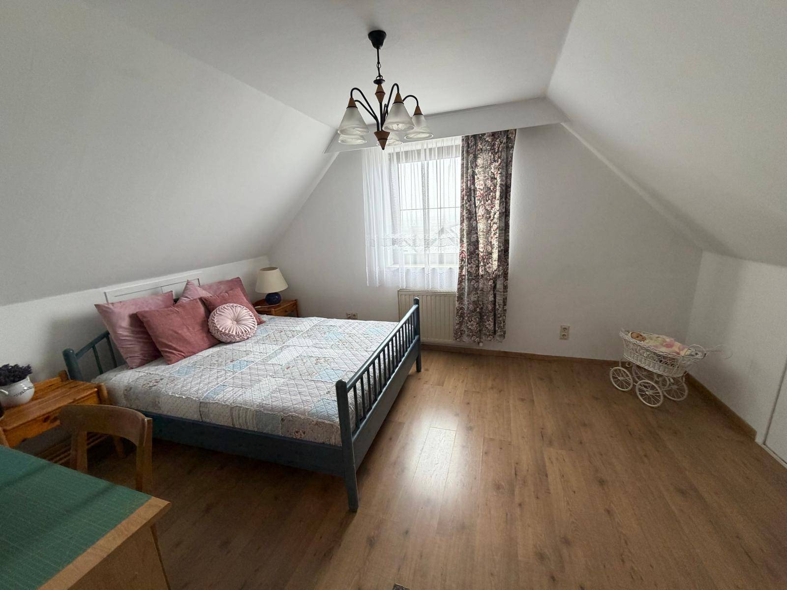Geräumiges Schlafzimmer im Dachgeschoss mit Holzboden, Bett und Fenster mit Vorhängen.