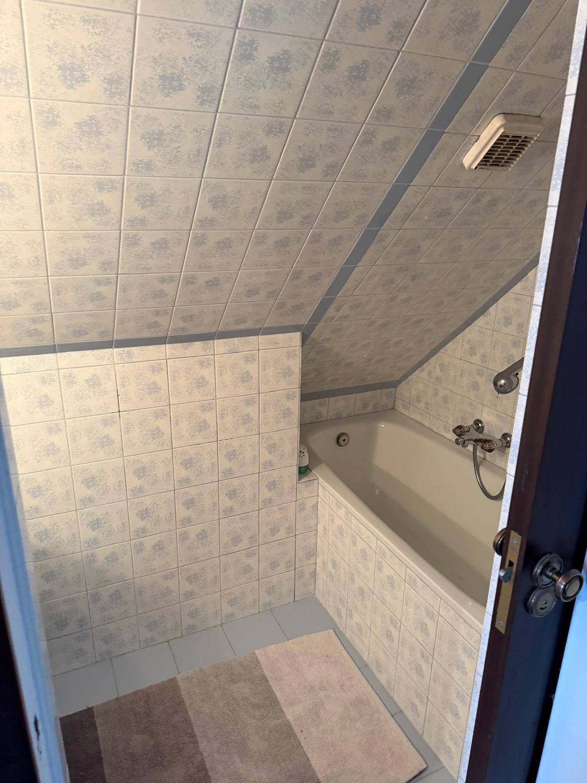 Badezimmer im Dachgeschoss mit blauen Fliesen, Badewanne und schräger Decke.