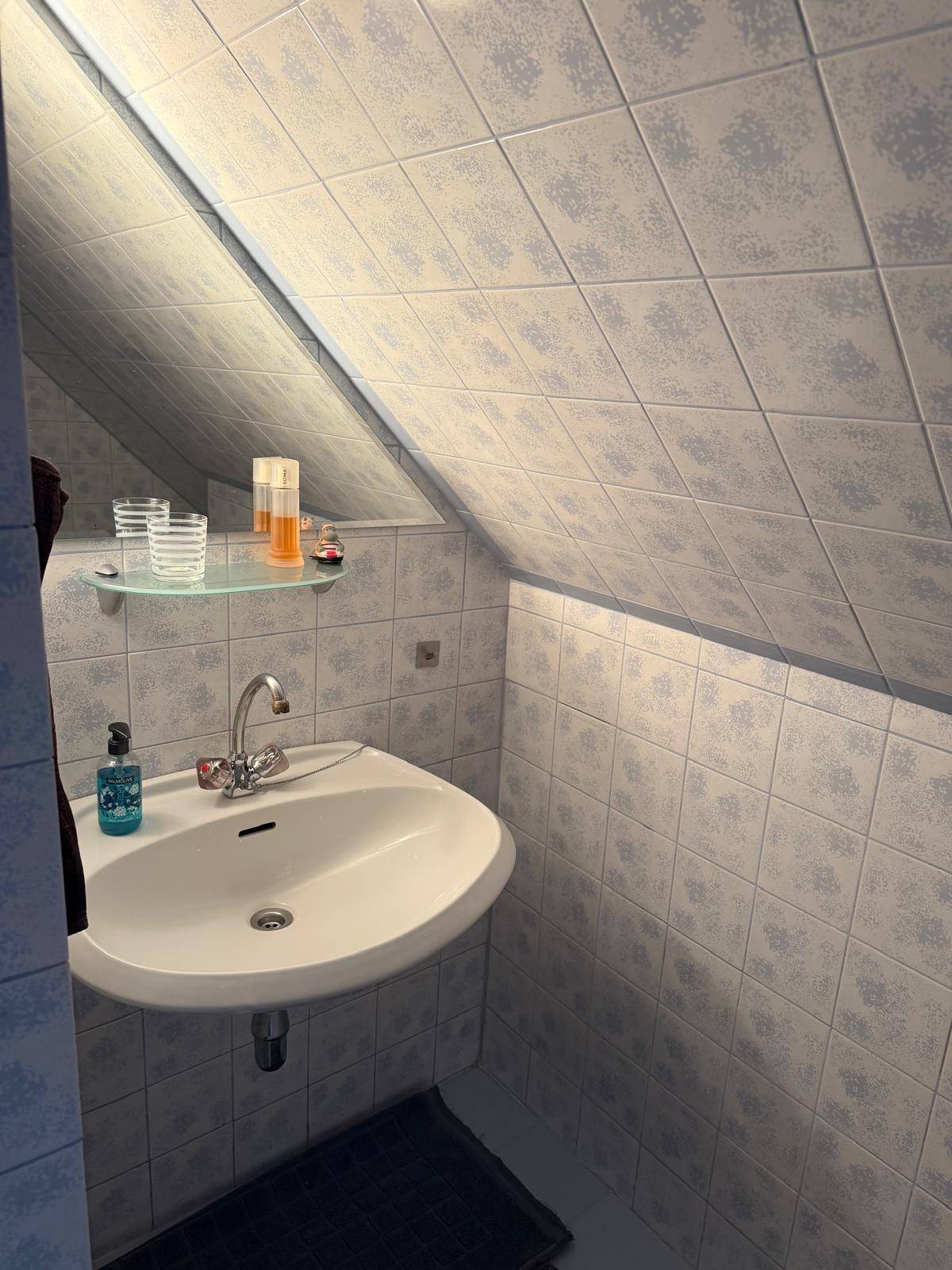 Waschbeckenbereich im Badezimmer mit Spiegel, Glasablage und blauen Fliesen.