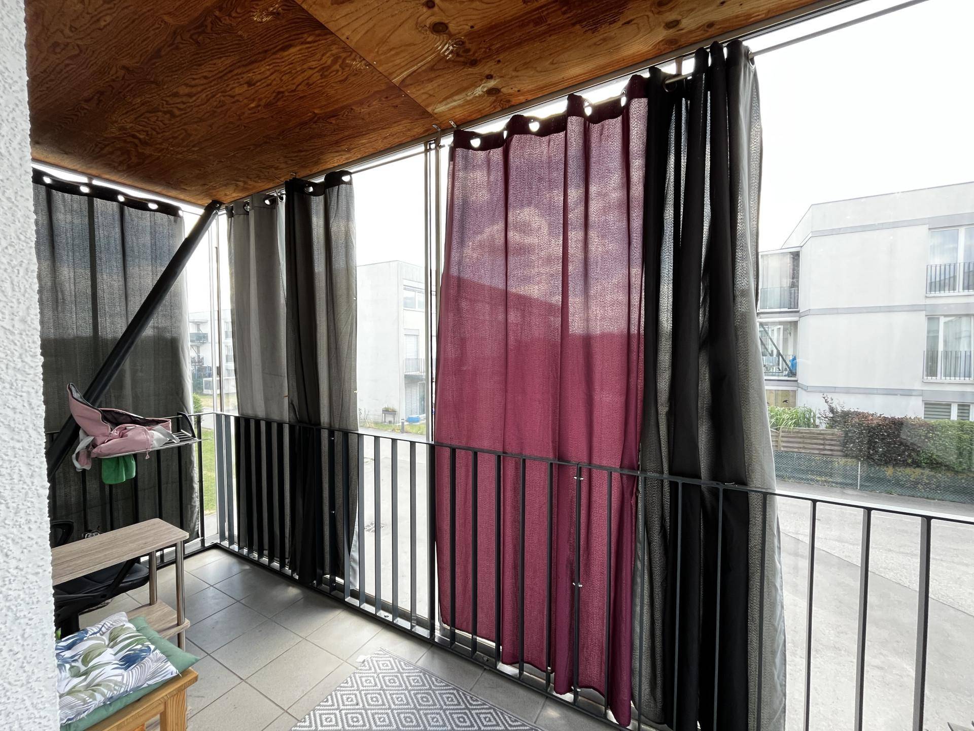 Verglaster Balkon mit Vorhängen, Holzdecke und Blick auf die umliegenden Gebäude.