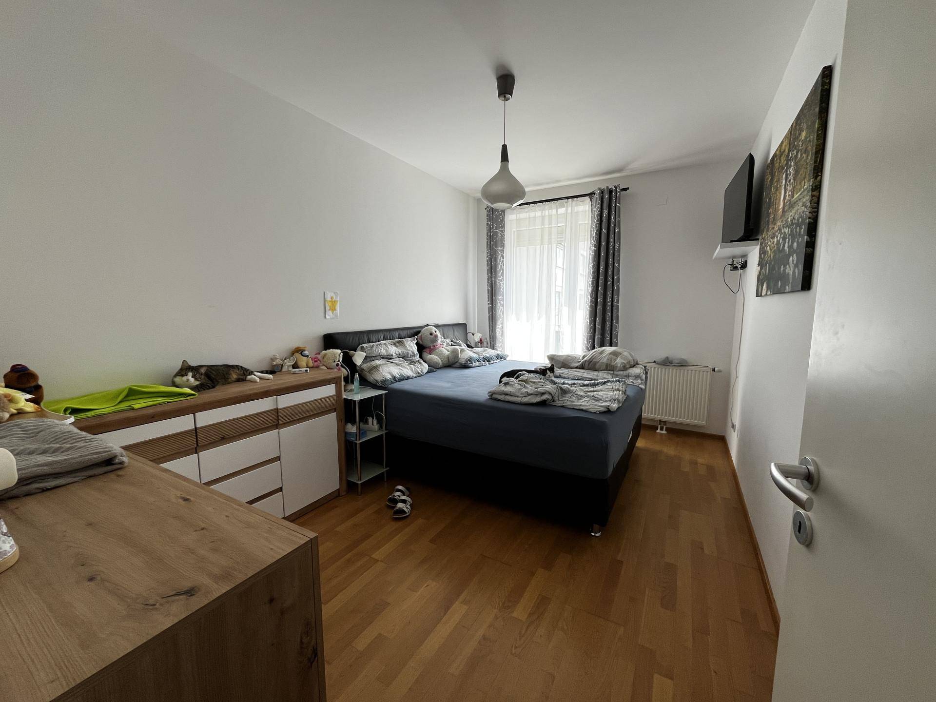 Helles Schlafzimmer mit Doppelbett, Kommode und Holzparkettboden.