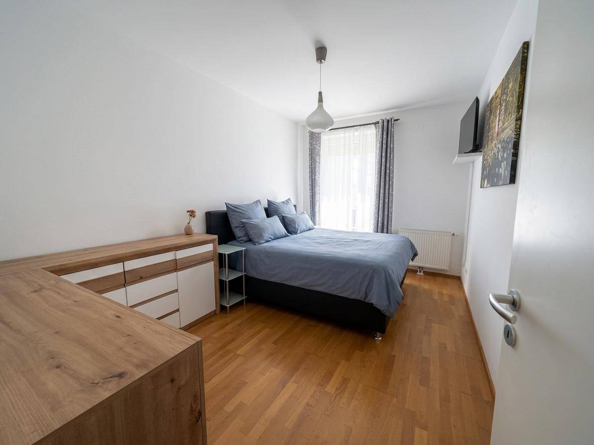 Schlafzimmer mit Bett, Kommode und hellem Holzfußboden.