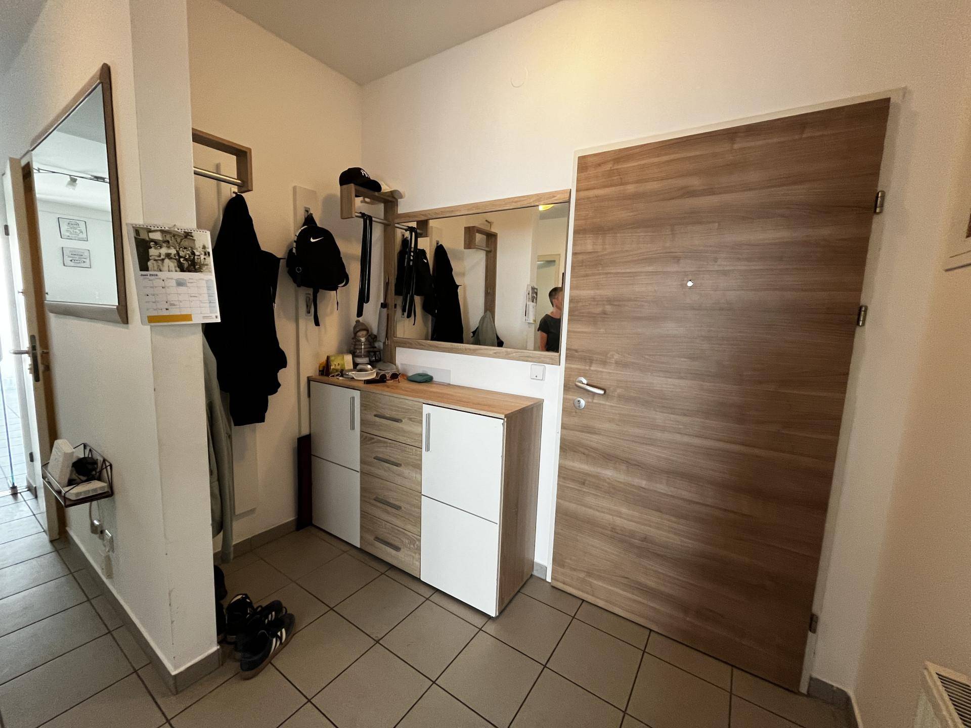 Eingangsbereich mit Holztür, Schuhschrank und großem Spiegel.