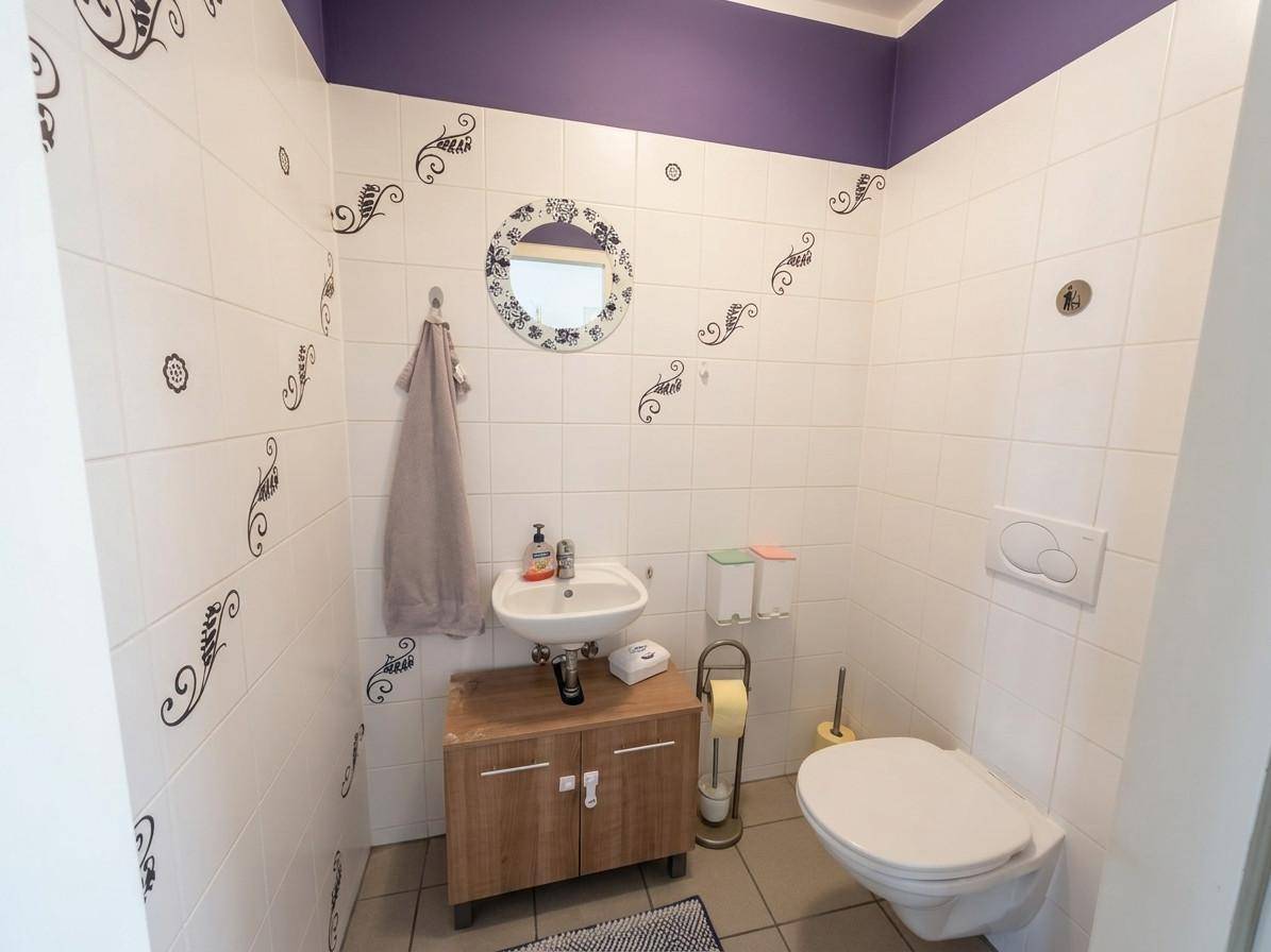 Gäste-WC mit Waschbecken, Toilette und dekorativen Fliesen sowie lila Wandfarbe.