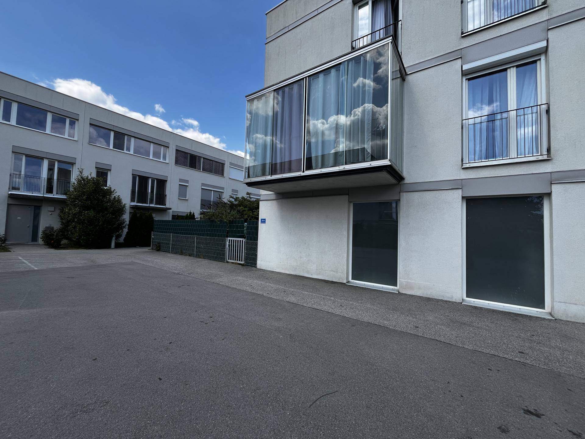 Außenansicht der Wohnanlage mit Parkplatz und angrenzenden Gebäuden.