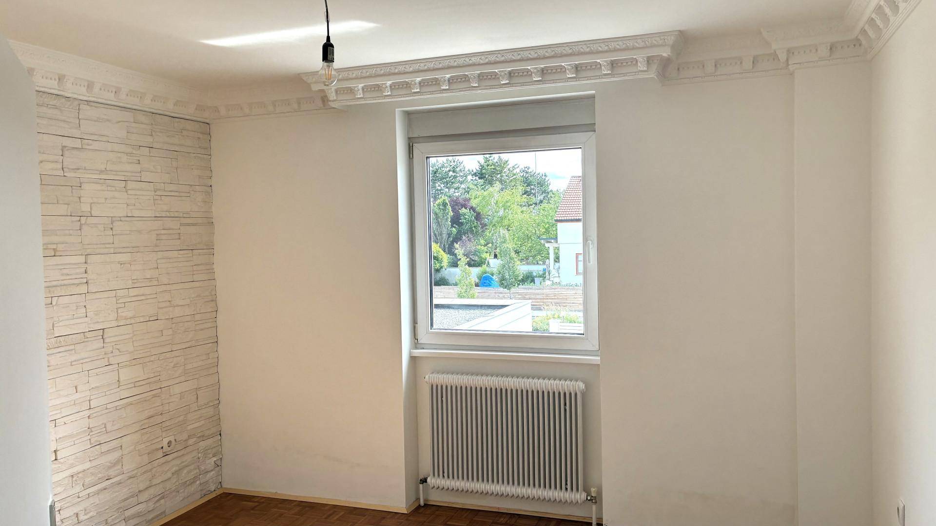 Heller Raum mit weiß gestrichenen Wänden, Fenster, Heizkörper und dekorativer Steinwand.