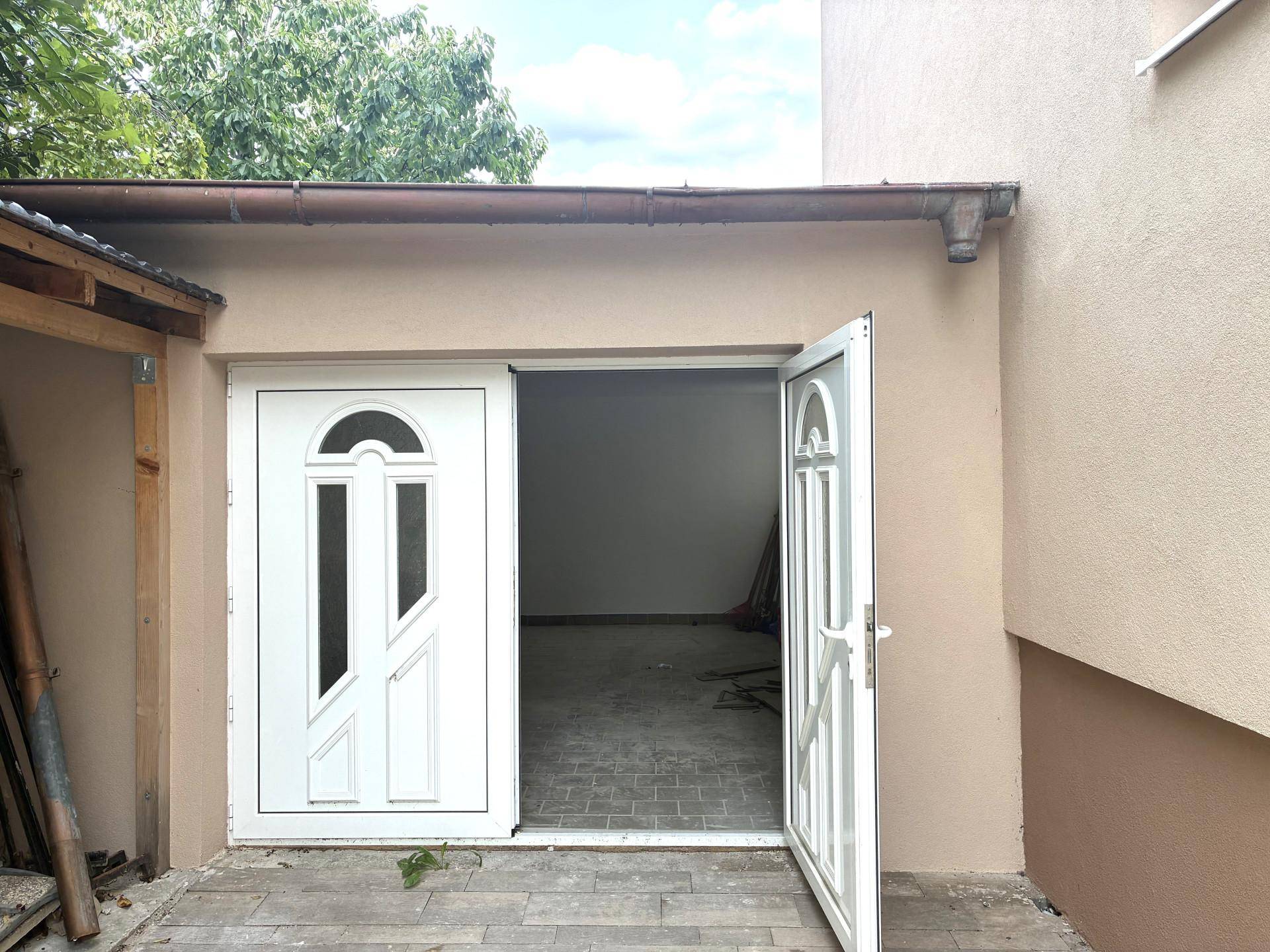 Zwei weiße Türen, eine offen, führen in einen unfertigen Raum, möglicherweise eine Garage.
