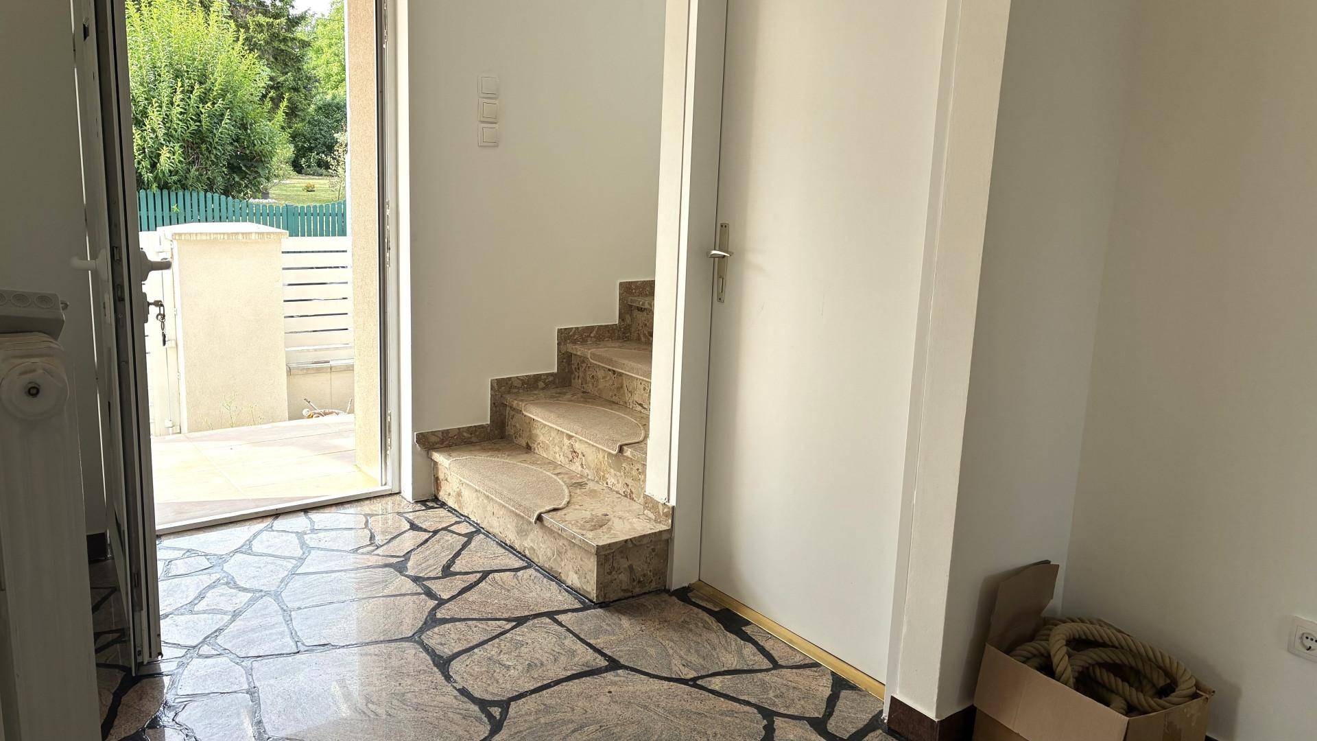 Eingangsbereich mit auffälligem Steinboden, Treppe und offener Tür zum Außenbereich.