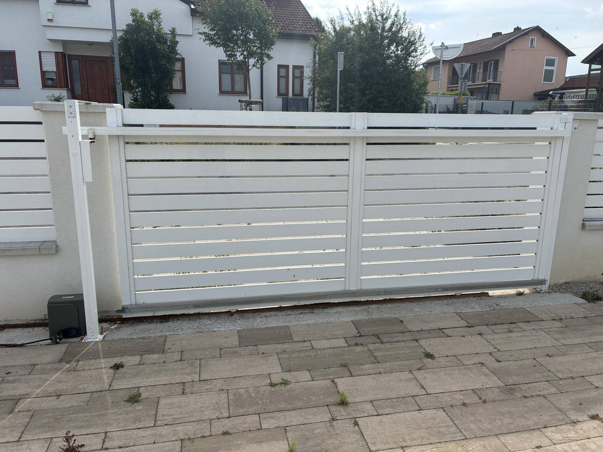 Weißes Schiebetor am Eingang des Grundstücks mit gepflastertem Vorplatz.
