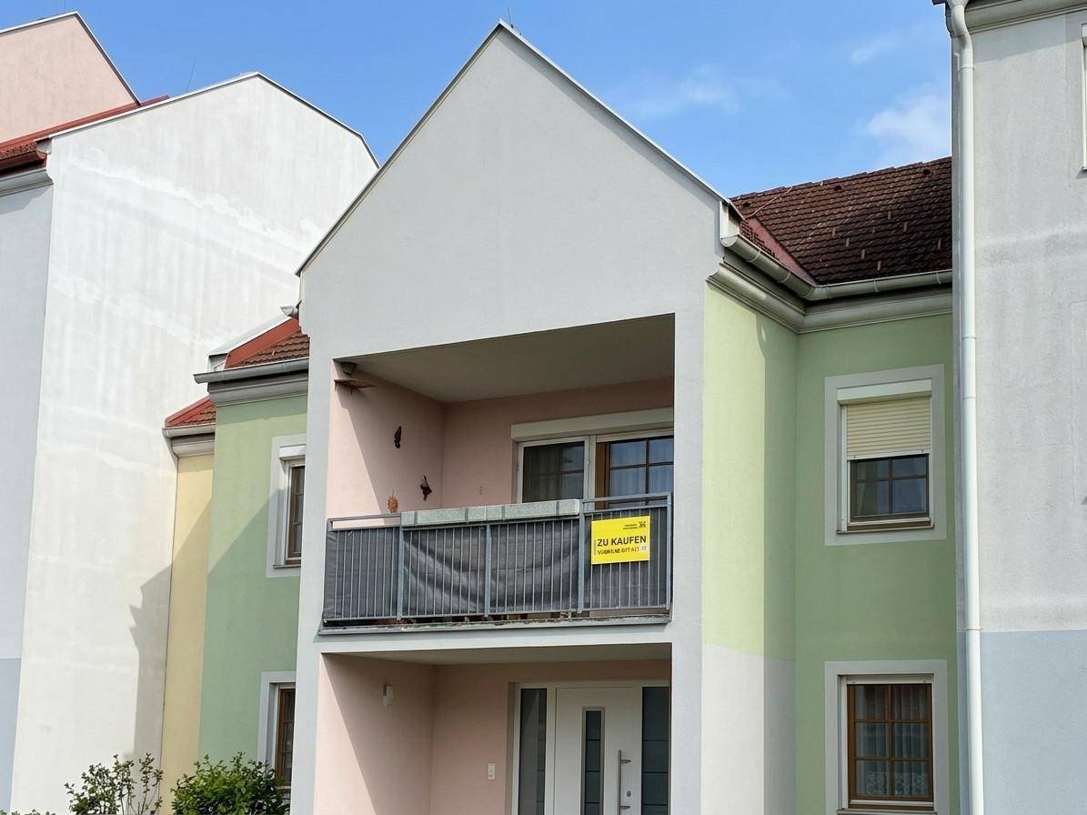 Fassade eines Mehrfamilienhauses mit pastellfarbenen Wänden, Balkon und Satteldach unter blauem Himmel.