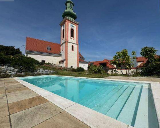 Außenpool mit Steinfliesen und Blick auf eine historische Kirche unter blauem Himmel.