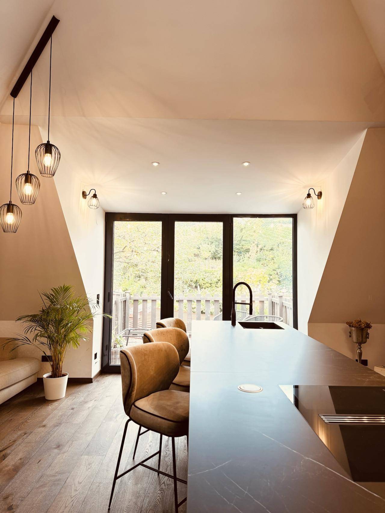 Moderne Küche mit dunkler Kücheninsel, Barhockern und Zugang zu einem Balkon mit Aussicht.