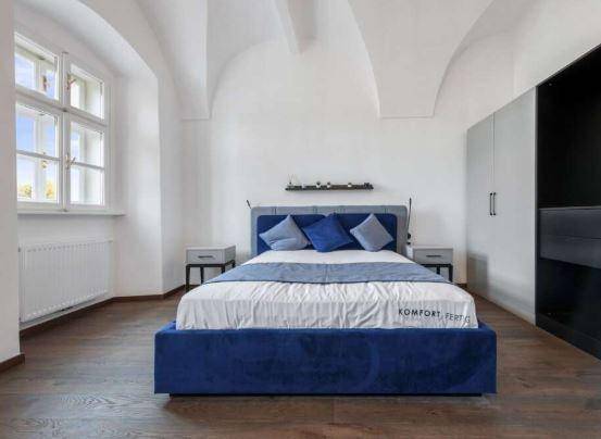 Helles Schlafzimmer mit blauem Polsterbett, hohen Gewölbedecken und großen Fenstern.
