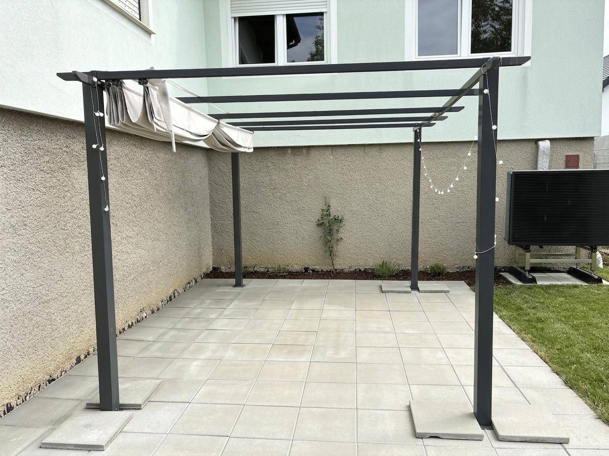 Geflieste Terrasse mit moderner Pergola und ausziehbarer Beschattung neben dem Haus.