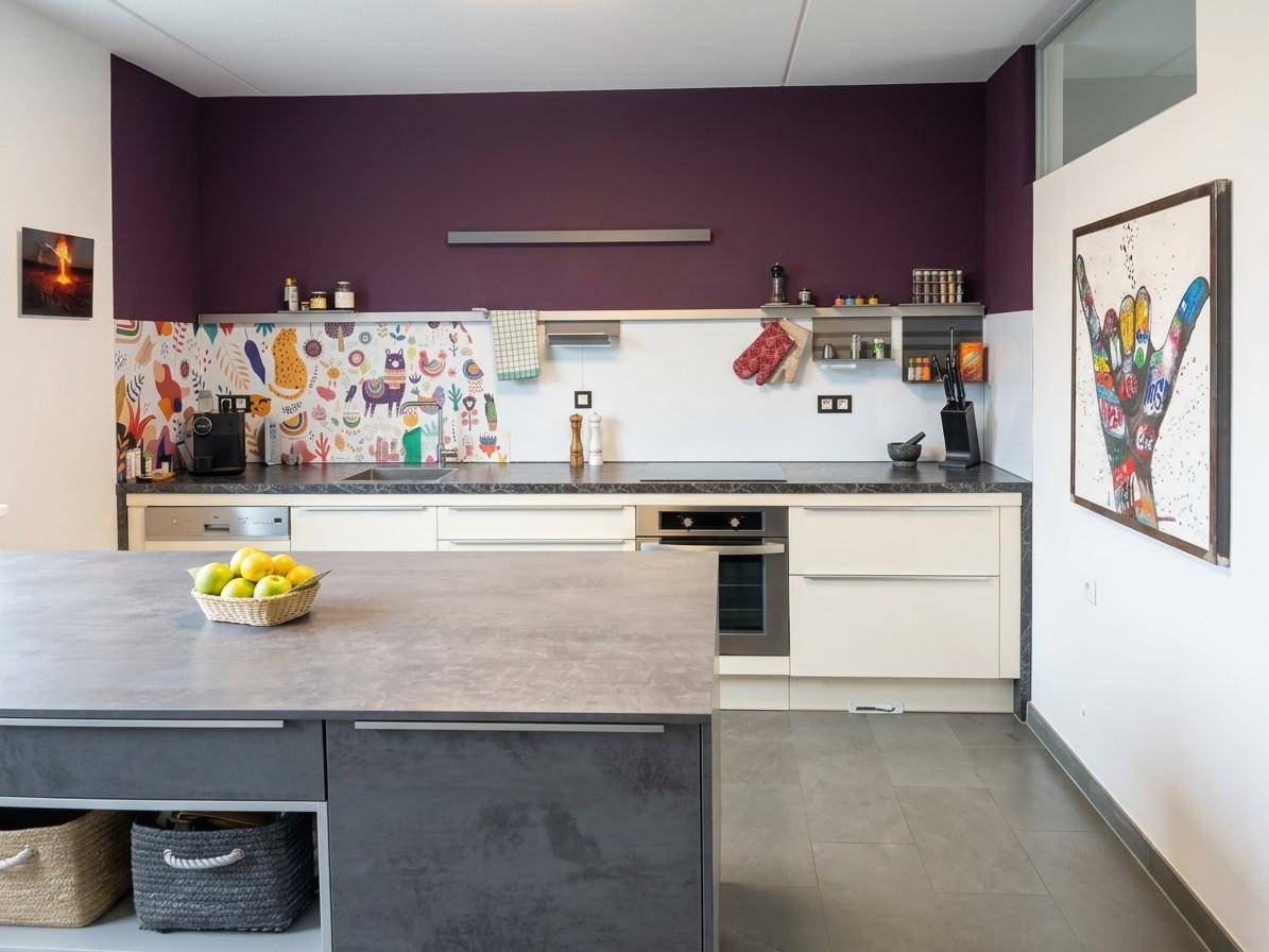 Moderne Küche mit lila Akzentwand, Kücheninsel und farbenfroher Spritzschutzverkleidung, ausgestattet mit Geräten.