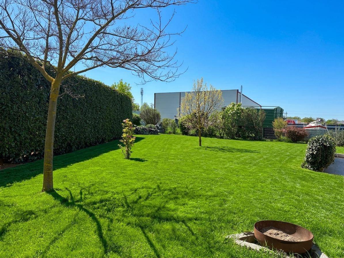 Große, gepflegte Rasenfläche mit Bäumen, einer hohen Hecke und einer Feuerschale im weitläufigen Garten.