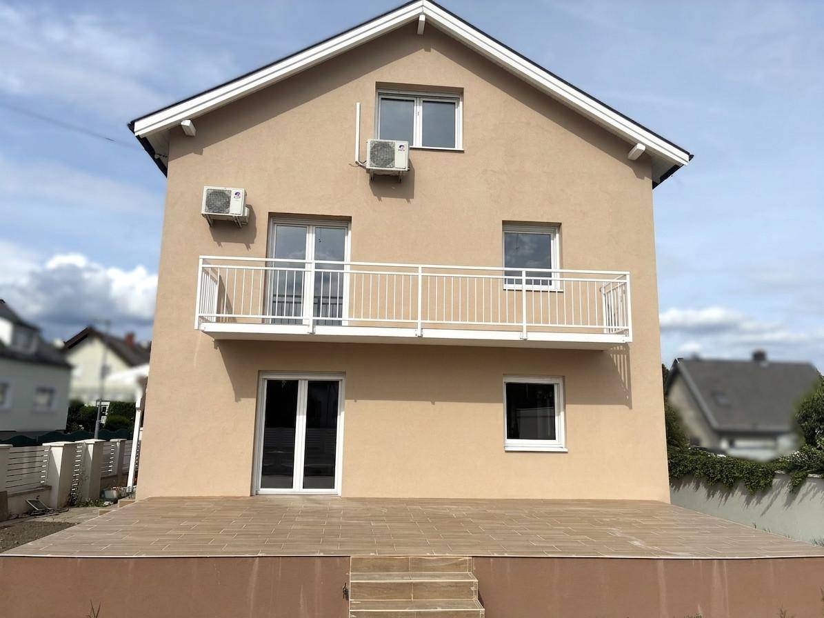 Rückansicht des Hauses mit einer großen gefliesten Terrasse und einem Balkon im Obergeschoss.