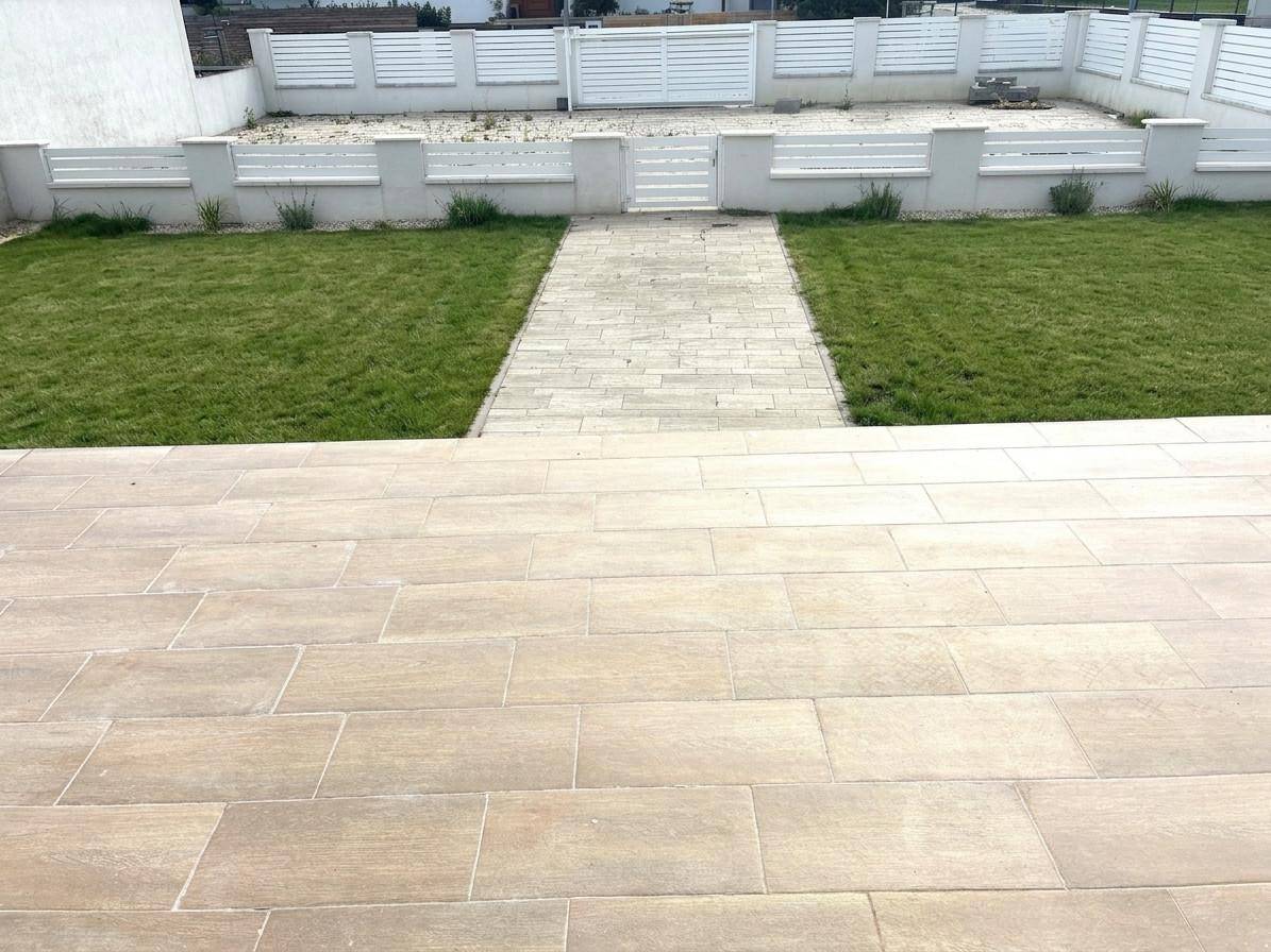 Geflieste Terrasse mit Blick auf den Gartenbereich und einen weißen Zaun im Hintergrund.