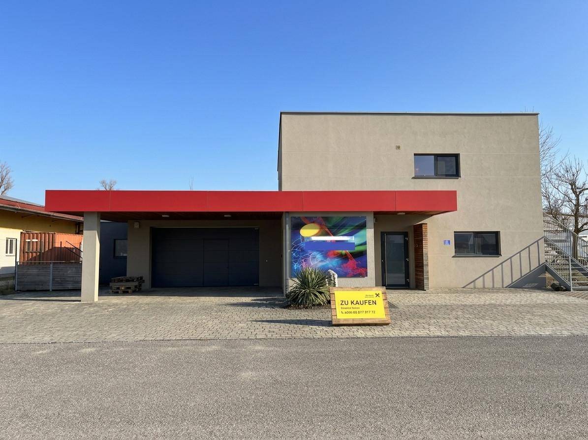Vorderansicht des modernen Gebäudes mit integrierter Garage, rotem Vordach und einem Verkaufsschild.