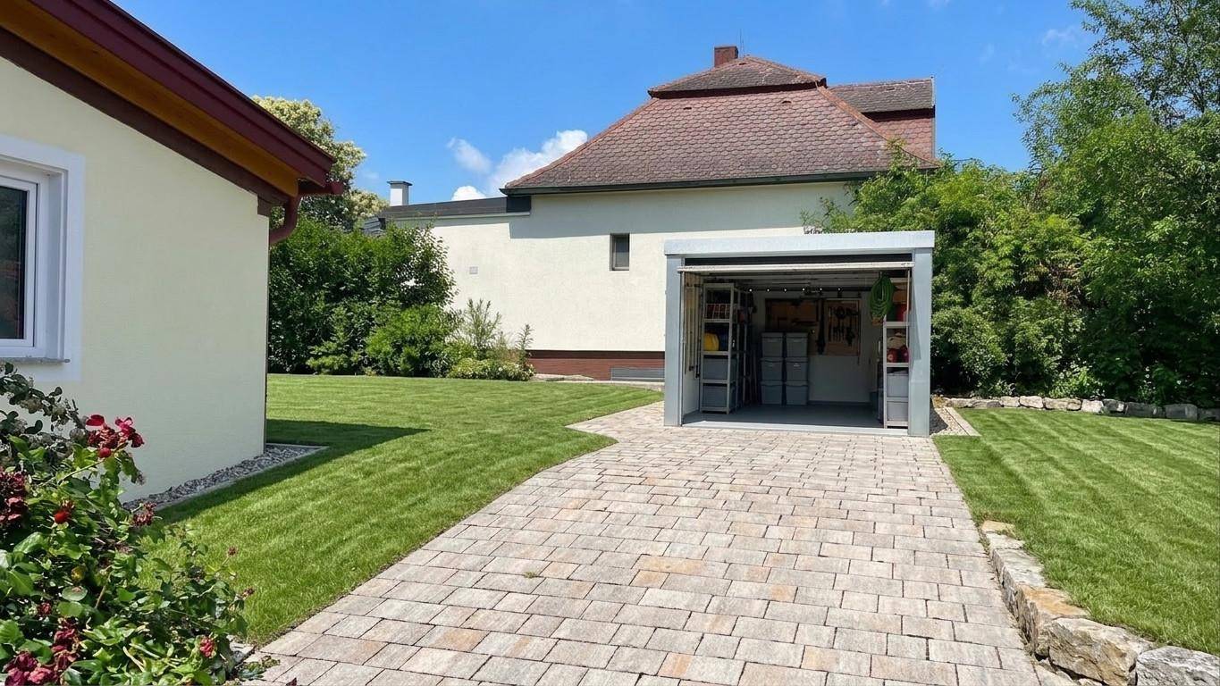 Gepflasterte Einfahrt führt zu einer modernen Garage, umgeben von gepflegtem Rasen und einem Wohnhaus im Hintergrund.