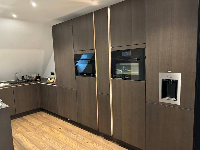 Moderne Einbauküche mit dunklen Holzfronten, integrierten Geräten und Holzboden.