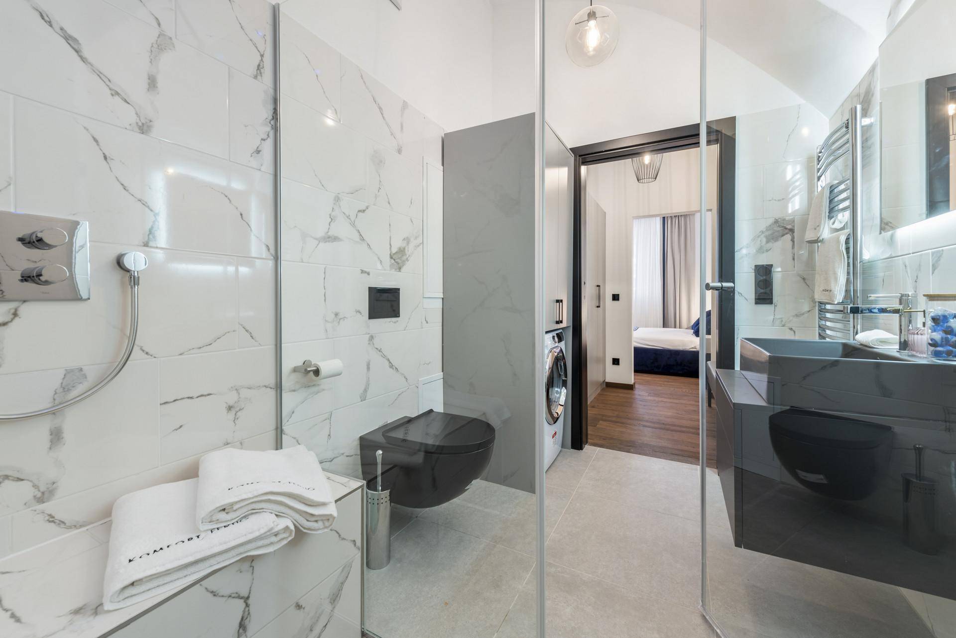 Modernes Badezimmer mit Marmorfliesen, wandhängender Toilette und Duschbereich, angrenzend an ein Schlafzimmer.