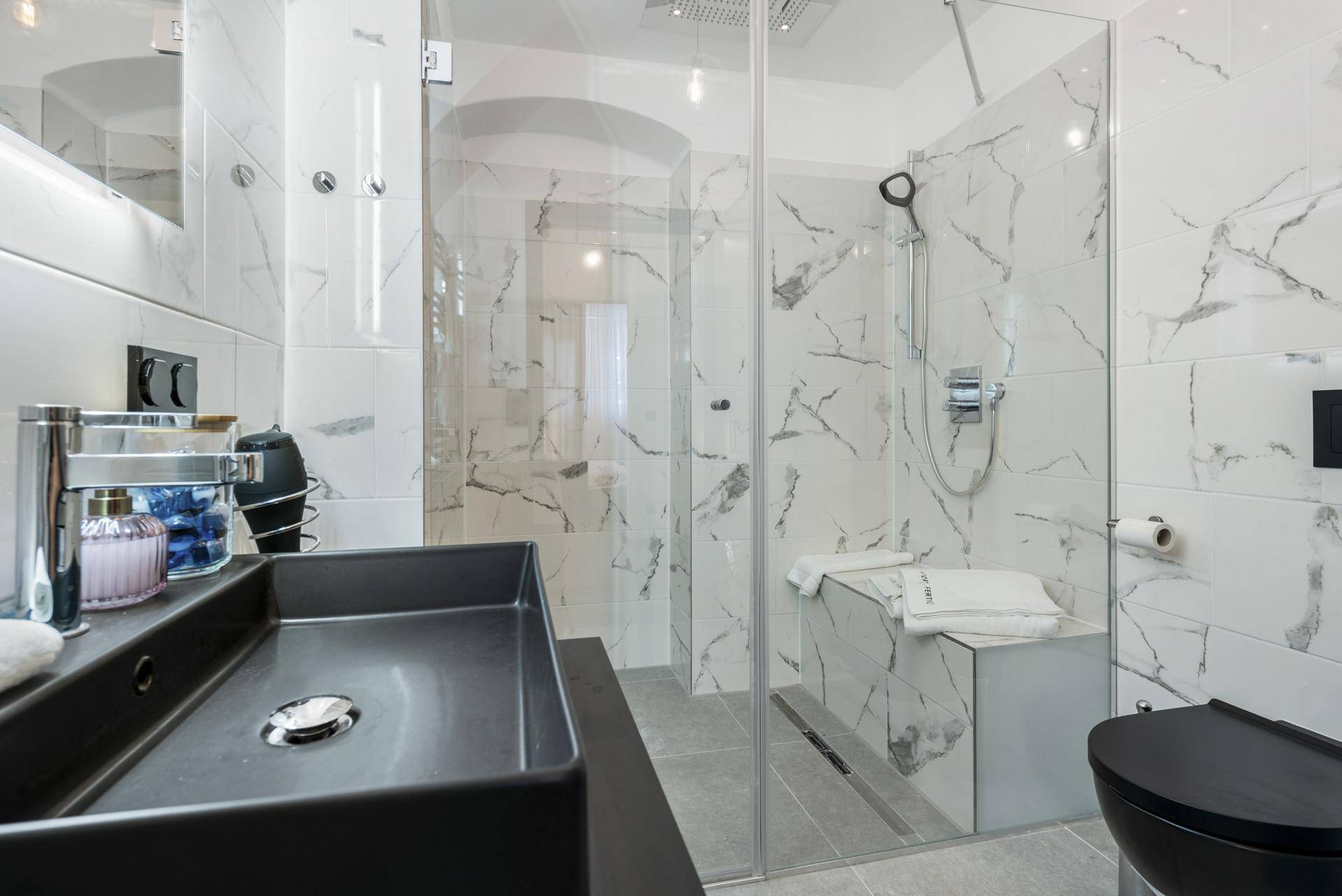 Modernes Badezimmer mit Marmorfliesen, großer begehbarer Dusche und schwarzem Waschbecken.
