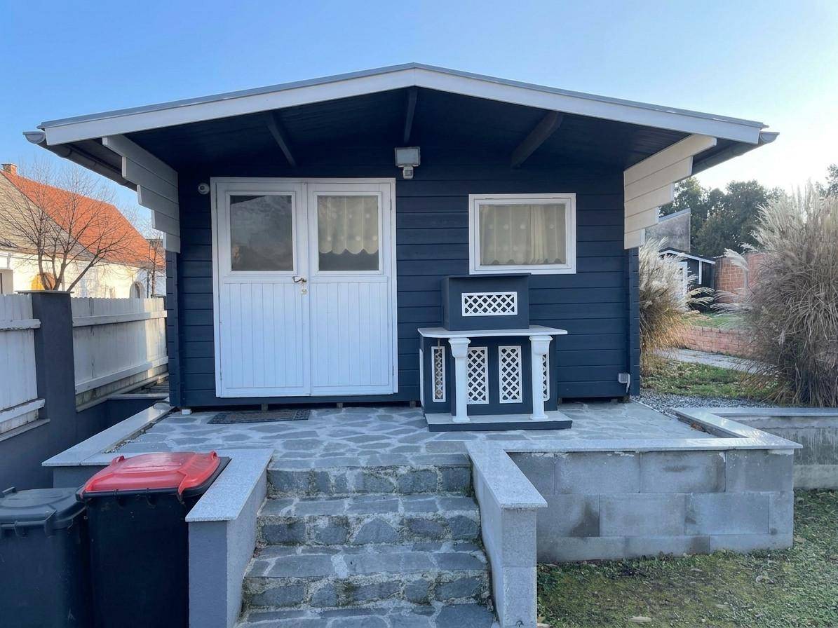 Kleines Gartenhaus mit dunkler Holzfassade und weißer Doppeltür im Außenbereich.