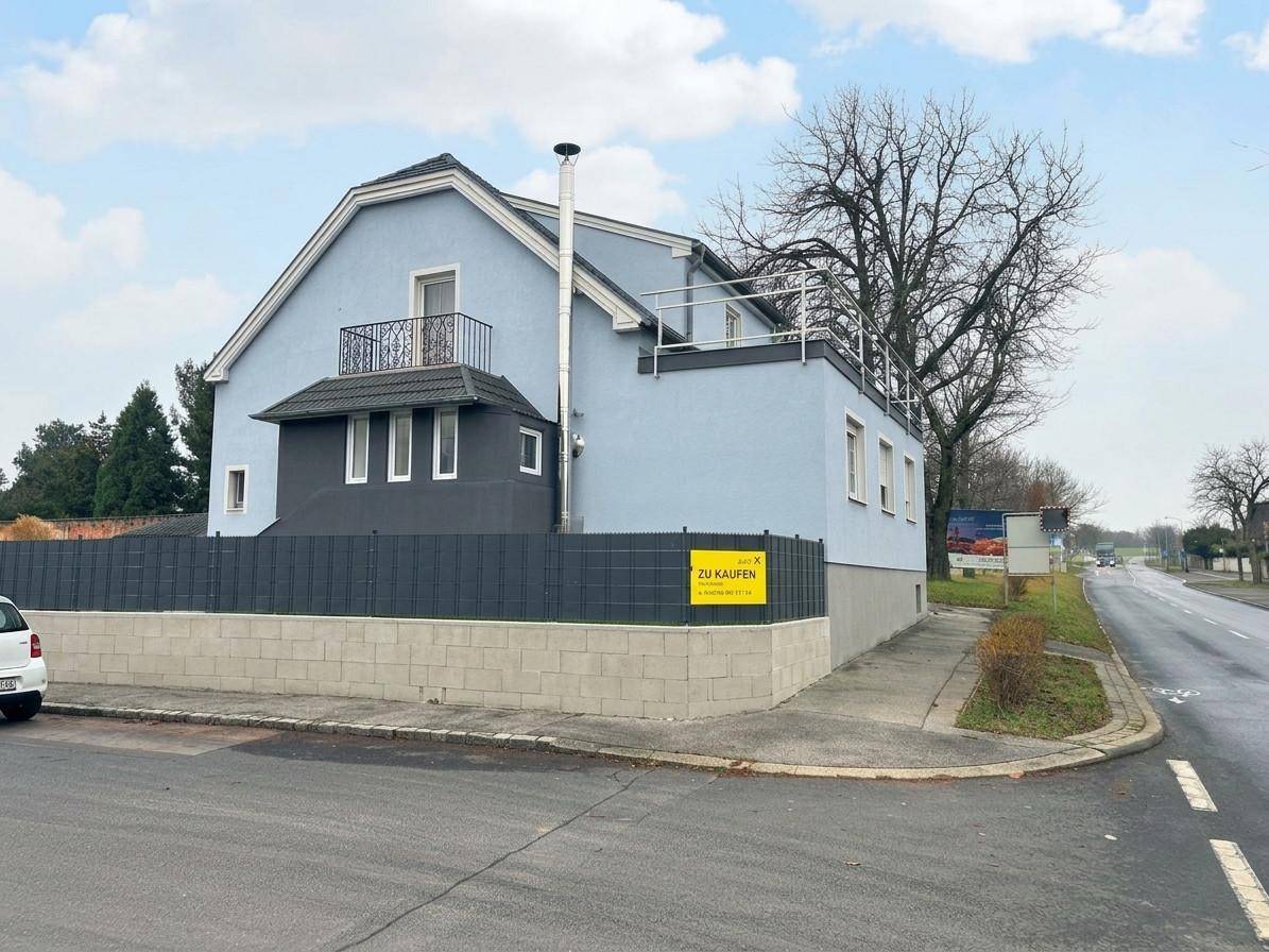 Seitenansicht des Hauses von der Straße mit Balkon und 'Zu Kaufen'-Schild.