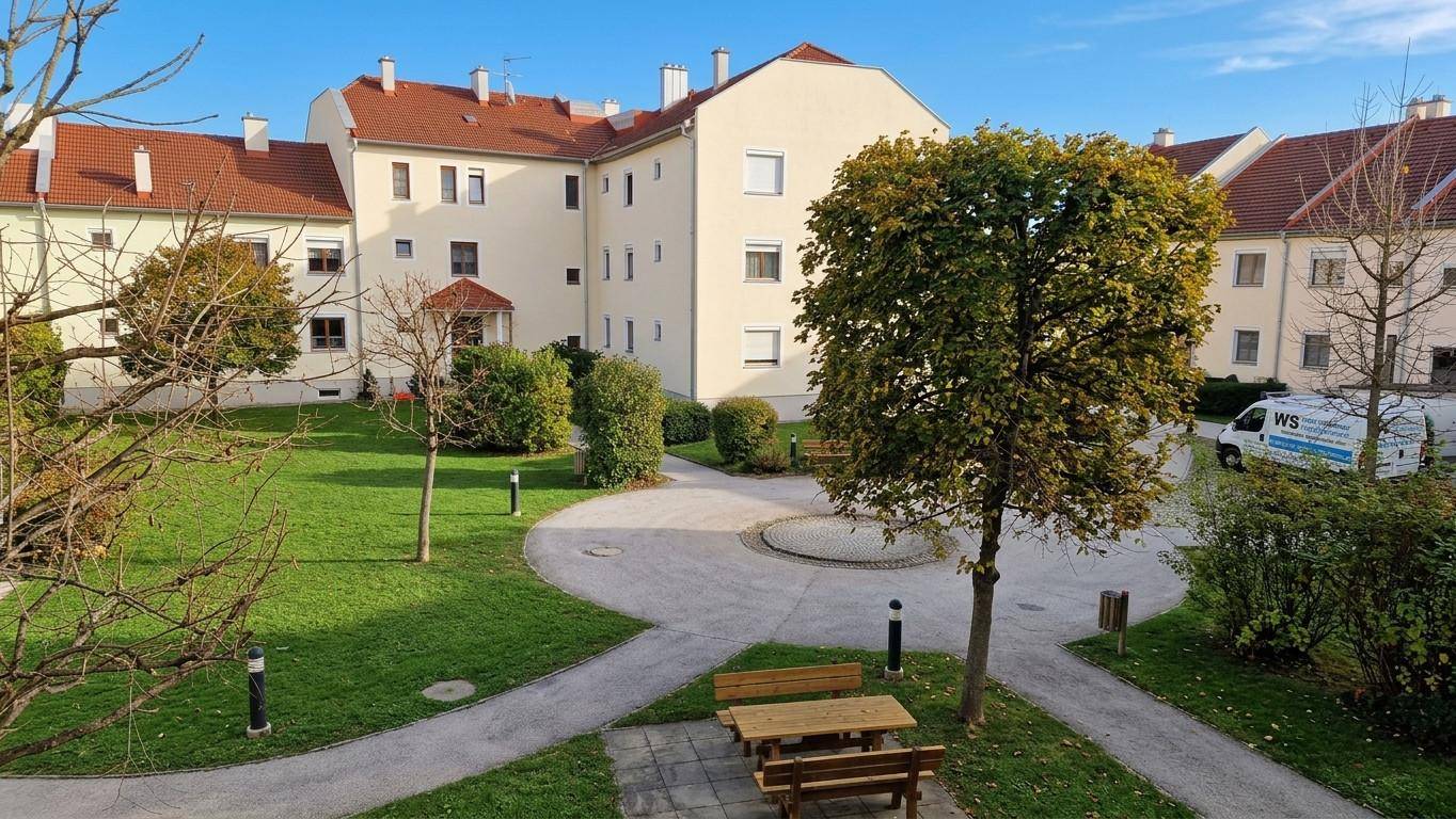 Gepflegter Innenhof einer Wohnanlage mit Grünflächen, Wegen und Sitzgelegenheiten.