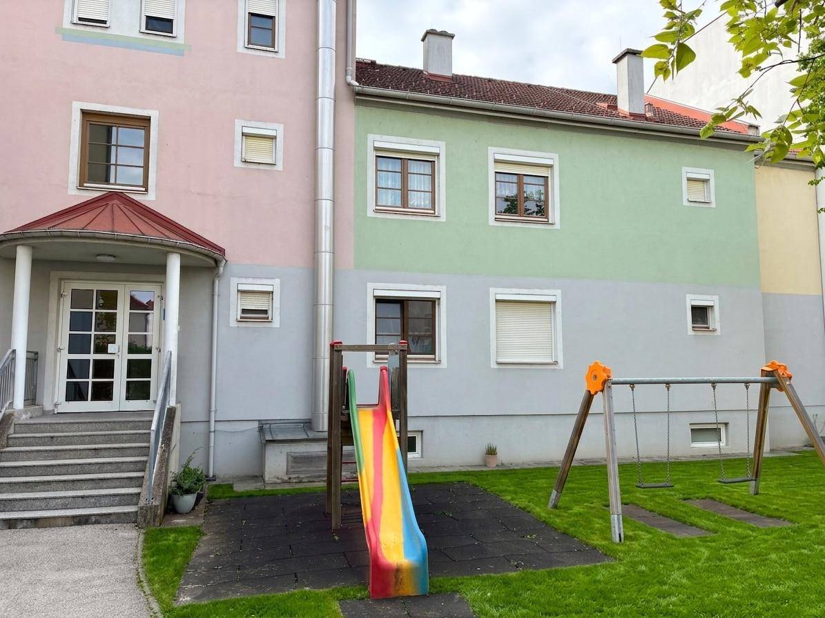 Mehrfamilienhaus mit farbiger Fassade und einem Spielplatz im Vorgarten für Kinder.