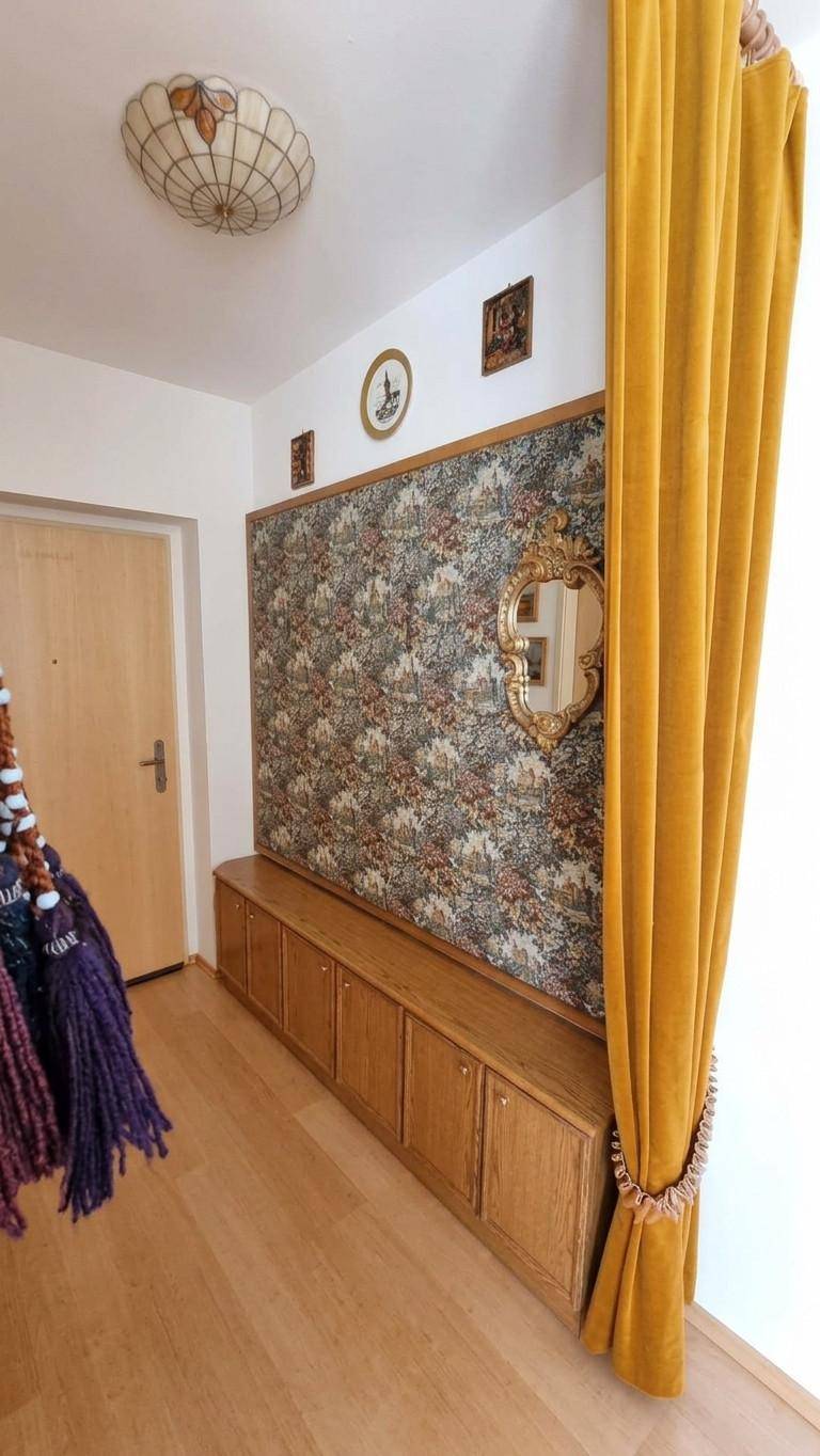 Dekorativer Wandbereich mit floraler Tapete, Holzschrank und gelbem Vorhang in einem Flur.