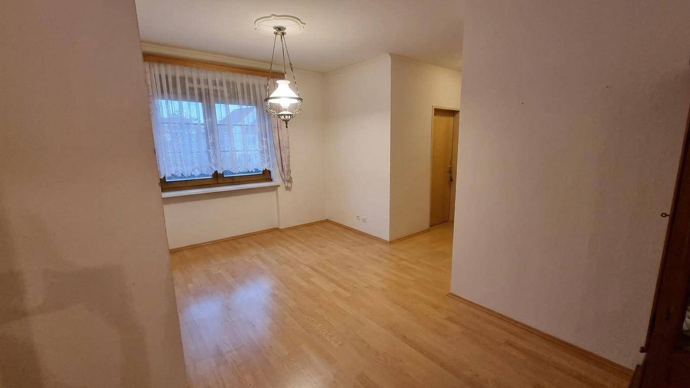 Leeres Zimmer mit hellem Parkettboden, Fenster und klassischer Hängelampe.