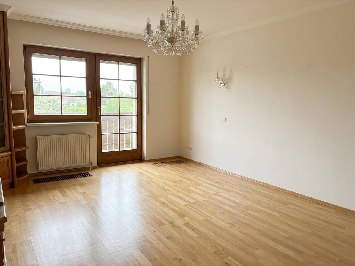 Geräumiges Wohnzimmer mit Parkettboden, Balkonzugang und elegantem Kronleuchter.